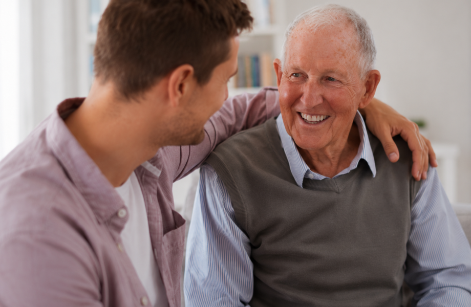 A caregiver checking in with an older man at home, sharing a smile